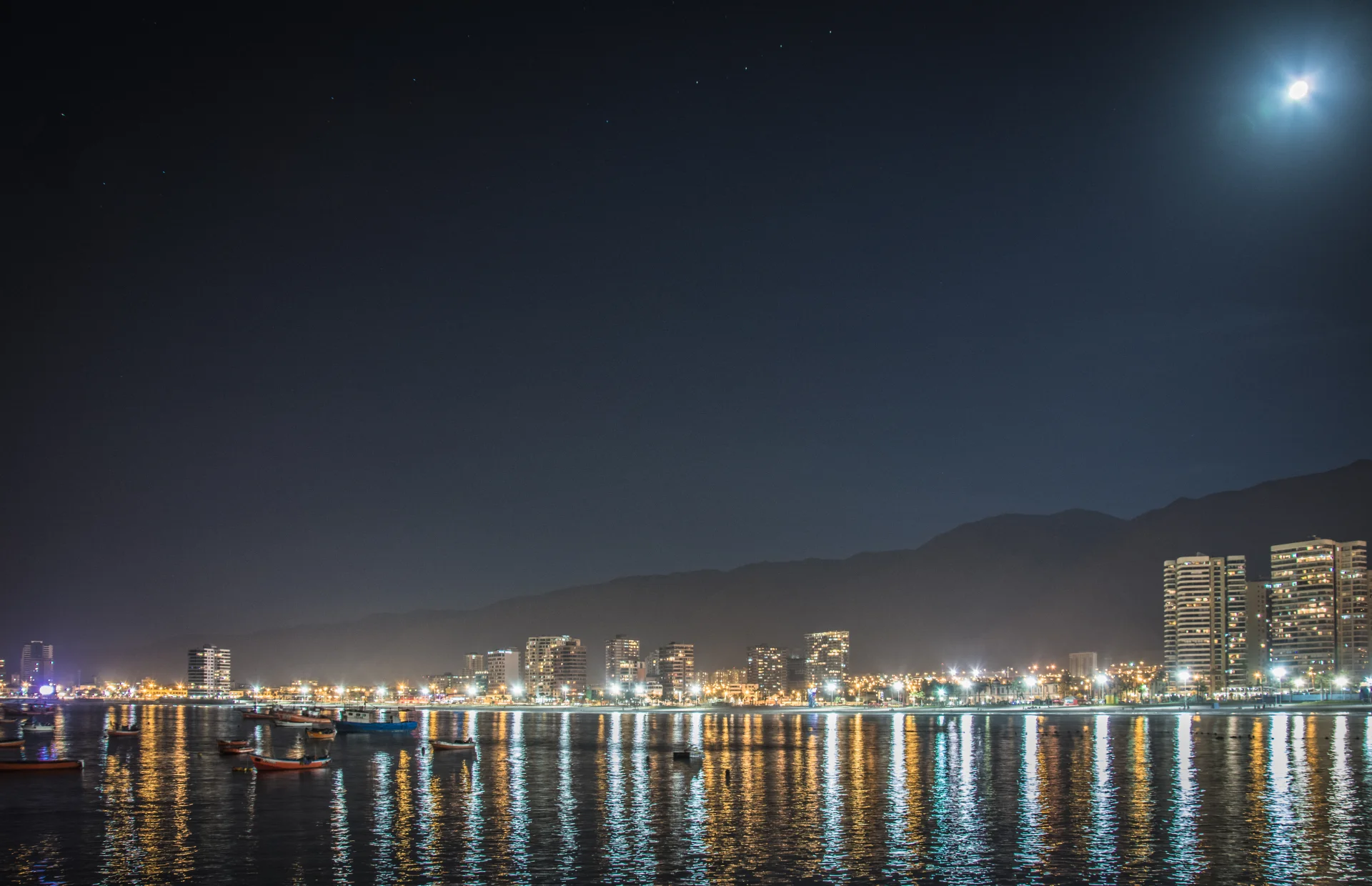 Bahía de Cavancha bajo la luna, con barcos y luces de Iquique reflejadas en el agua